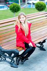 Fototapeta na wymiar Girl in red coat sit on bench in park