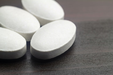 Fototapeta na wymiar White pills of calcium, vitamin supplement, medical tablets at wooden table, macro image