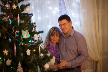 Young couple is standing at Christmas tree with fairy lights