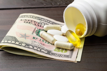 Yellow capsules of omega-3 in bottle, white capsules of glucosamine, white pills of calcium and dollars banknote at wooden table