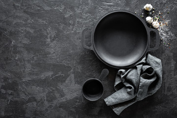 Empty cast-iron pan with cutlery on dark background for restaurant menu, top view