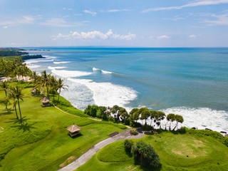 Aerial view to golf club with green hills, ocean and many palm trees near Tanah lot temple, Bali...