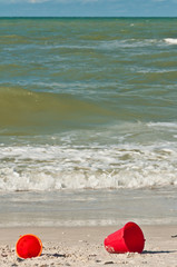 Two red children's pails in the sand at the shores edge on a rough, windy day at a tropical beach on the Gulf of Mexico