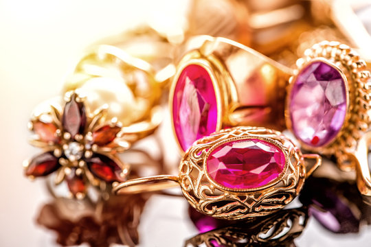Elegant luxury composition of gold jewelry with ring with red amethyst and ruby gemstone and diamonds on light background close-up macro and reflection