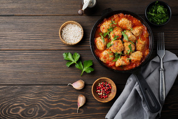 Meatballs in tomato sauce garlic and parsley in an iron frying pan on a dark brown wooden background. Selective focus. Top view. Copy space.
