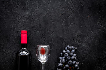 Taste red wine. Bottle of red wine, glass and black grape on black stone background top view copyspace