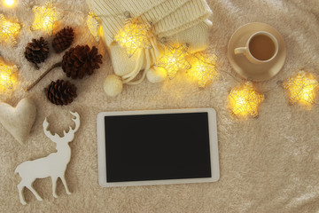 Cup of coffee next to tablet device with empty screen over cozy and warm fur carpet. Top view.
