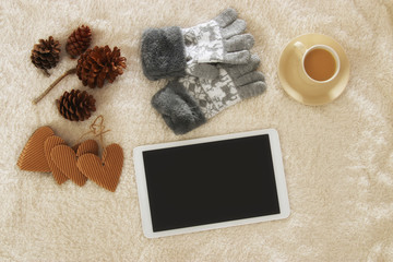 Fototapeta na wymiar Cup of coffee next to tablet device with empty screen over cozy and warm fur carpet. Top view.