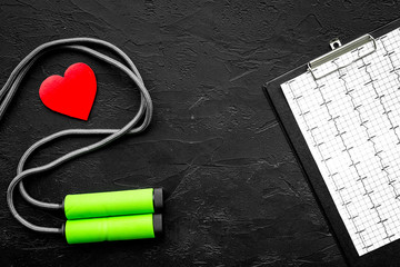 Prevent heart disease. Heart sign, cardiogram, jump rope on black background top view copyspace