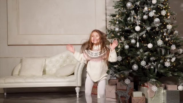 Child girl is joying for onset of Christmas, skipping and waiting to open boxes with gifts. Traditional annually celebrating of New year and Christmas, childrens fest.