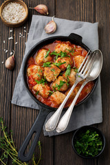 Meatballs in tomato sauce garlic and parsley in an iron frying pan on a dark brown wooden background. Selective focus. Top view. Copy space.
