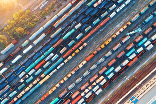 Fototapeta Top view of colorful cargo trains. Aerial view from flying drone of colorful freight trains on the railway station. Wagons with goods on railroad. Heavy industry. Industrial conceptual scene. Vintage