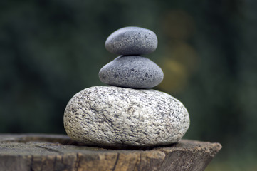 Three zen stones pile on wooden stump, white and grey meditation pebbles tower
