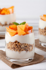 Persimmon creamy trifle in beautiful glasses, fresh ripe fruit slices on white wooden background. Healthy vegetarian food. Delicious dessert. Close up photography. Selective focus.