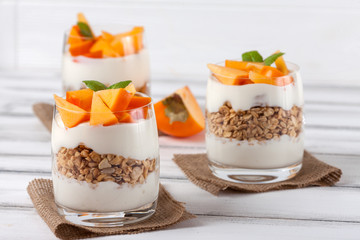 Persimmon creamy trifle in beautiful glasses, fresh ripe fruit slices on white wooden background. Healthy vegetarian food. Delicious dessert. Close up photography. Selective focus.