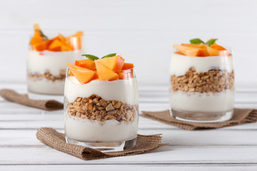 Persimmon creamy trifle in beautiful glasses, fresh ripe fruit slices on white wooden background. Healthy vegetarian food. Delicious dessert. Close up photography. Selective focus.