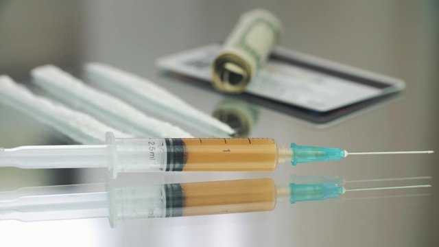 Cocaine powder, medicine syringe on the glass table 