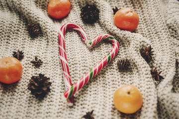stylish peppermint candy cane in heart shape and pine cones and anise with tangerine on rustic knitted sweater background top view, space for text.  seasonal greetings.  merry christmas concept