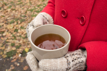 Women's hands in warm gloves hold a cup of tea