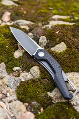 Pocket knife. Vertical shot. A knife on a stone and a moss.