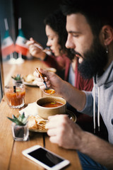 A handsome male hipster with a beard eating a hot soup at a cafe, lunch break.