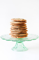 Stack of freshly baked, homemade  traditional American Chocolate Chip Cookies on glass cake stand on white background
