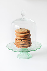 Stack of freshly baked, homemade  traditional American Chocolate Chip Cookies on glass cake stand on white background