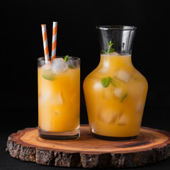 Mandarin cocktail with ice and mint in beautiful glasses and jug, fresh ripe citrus on white wooden background. Sweet orange juice. Close up photography. Selective focus