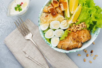 Traditional Caesar Salad with quail eggs and pine nuts in a light ceramic bowl On a gray stone or concrete background. Lunch bowl. Selective focus. Top view.