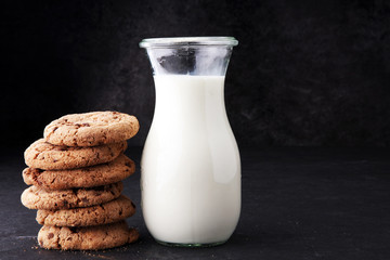 Chocolate chip cookies with milk on dark grey table