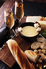 Gourmet Swiss fondue dinner on a winter evening with assorted cheeses on a board alongside a heated pot of cheese fondue with two forks dipping bread and white wine or champagne