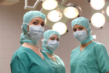Fototapeta na wymiar A group of three young women pose in a medical operation theater. Fully dressed as theater nurses with face masks and green sterile medical work clothing.