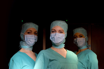 Fototapeta na wymiar A group of three young women pose in a medical operation theater. Fully dressed as theater nurses with face masks and green sterile medical work clothing.