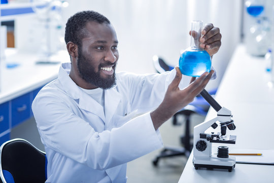 Chemical analysis. Positive nice smart scientist holding a flask and looking at it while doing a chemical analysis