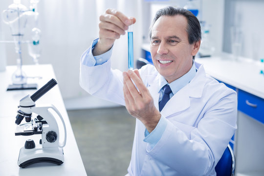 Chemical reagent. Positive cheerful ice man holding a test tube and looking at the liquid in it while doing chemical research