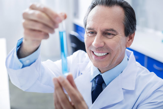 This is success. Cheerful nice positive man looking at the test tube and smiling while being happy about his success