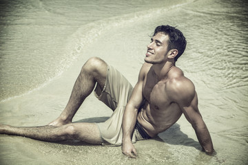 Handsome young man laying down on a beach in Phuket Island, Thailand, shirtless wearing boxer shorts, showing muscular fit body