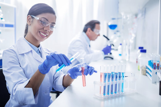 Modern lab. Joyful positive smart woman sitting at the table and wearing protective glasses while working with chemical reagents