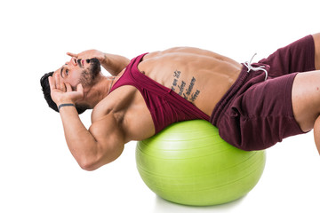 Attractive bodybuiler man exercising abs on an exercise ball in studio shot, isolatedo on white. Tattoo says Winning is not about not falling, but about not staying down