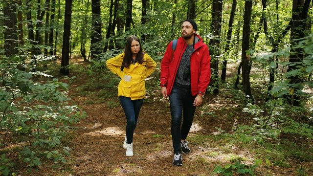 Young couple walking in the forest with backpacks. Woman having a backache and stoping tired. Outdoors