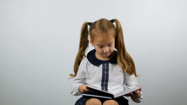 Bored cute girl opens the book and looks at the book. First-grade girl holding a book and reading.