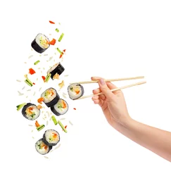 Fotobehang Vallende stukjes sushi en sushi roll met houten eetstokjes in vrouwelijke hand © Krafla
