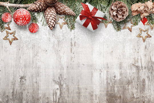 Christmas background with pine cones, fir branches, ornaments and gifts covered with snow. Old white wooden desk with Christmas decorations above, free space for text