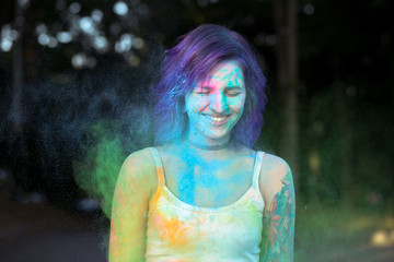 Happy woman with purple hair covered with blue Holi powder at the park