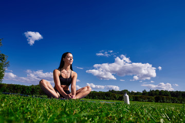 Girl sits in Park on a background of clear sky and enjoy the sunlight.