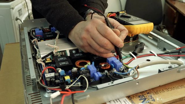 Service center. Electronics repair shops. A man repairs the hob. Multimeter.