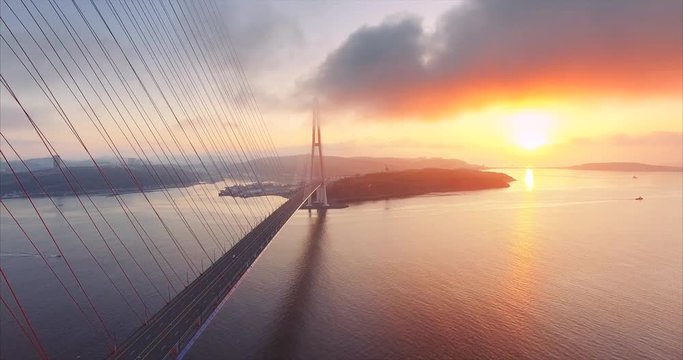 Flying backwards, great aerial view of Russian island and cable-stayed Russian Bridge across the Eastern Bosphorus strait in Vladivostok, Russia. Amazing bright sunrise