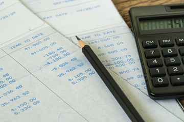 Financial office salary tax calculation or review concept with black calculator and pencil on salary revenue slips with numbers put on table