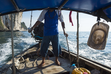 Obraz premium Scenic view from a traditional thai longtail boat as it passes by iconic karst mountain islands.