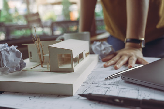Closeup image of a stressed architects thinking and drawing shop drawing paper with architecture model and laptop on table while fail